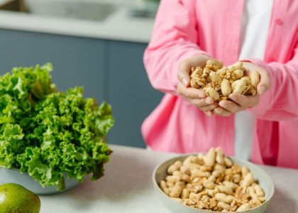 Hands presenting peanuts with a bowl, lettuce, avocado, and tomato nearby on kitchen counter.