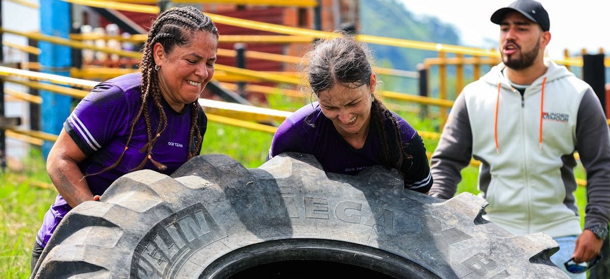 Two women and a man engage in an outdoor fitness session flipping a large tire.