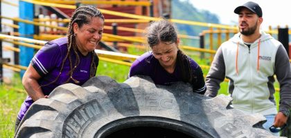 Two women and a man engage in an outdoor fitness session flipping a large tire.