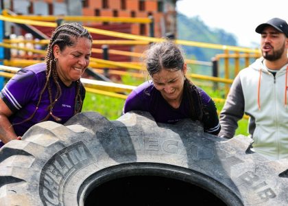 Two women and a man engage in an outdoor fitness session flipping a large tire.